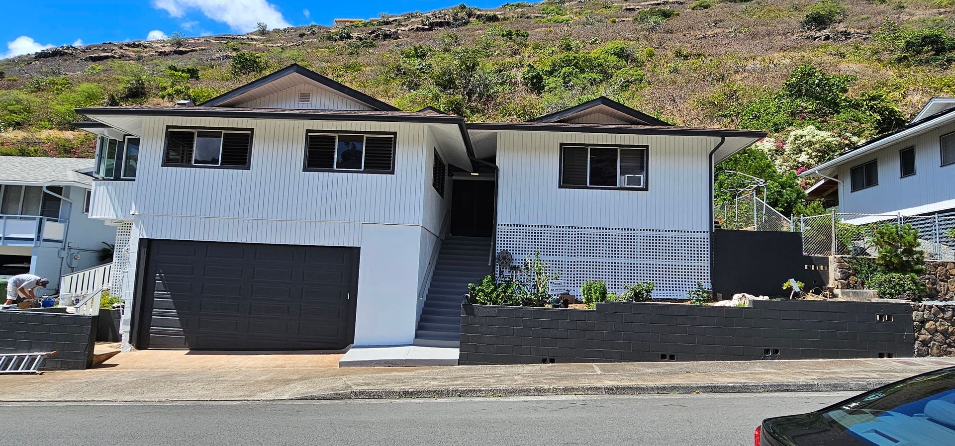 A car is parked in front of a white house on a hill.