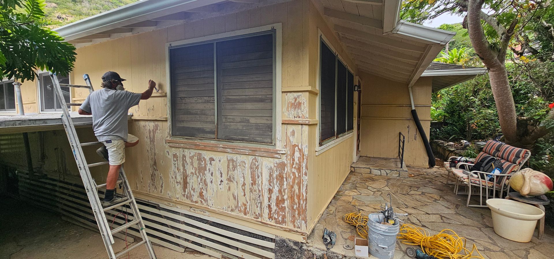 A man is painting the side of a house with a ladder.