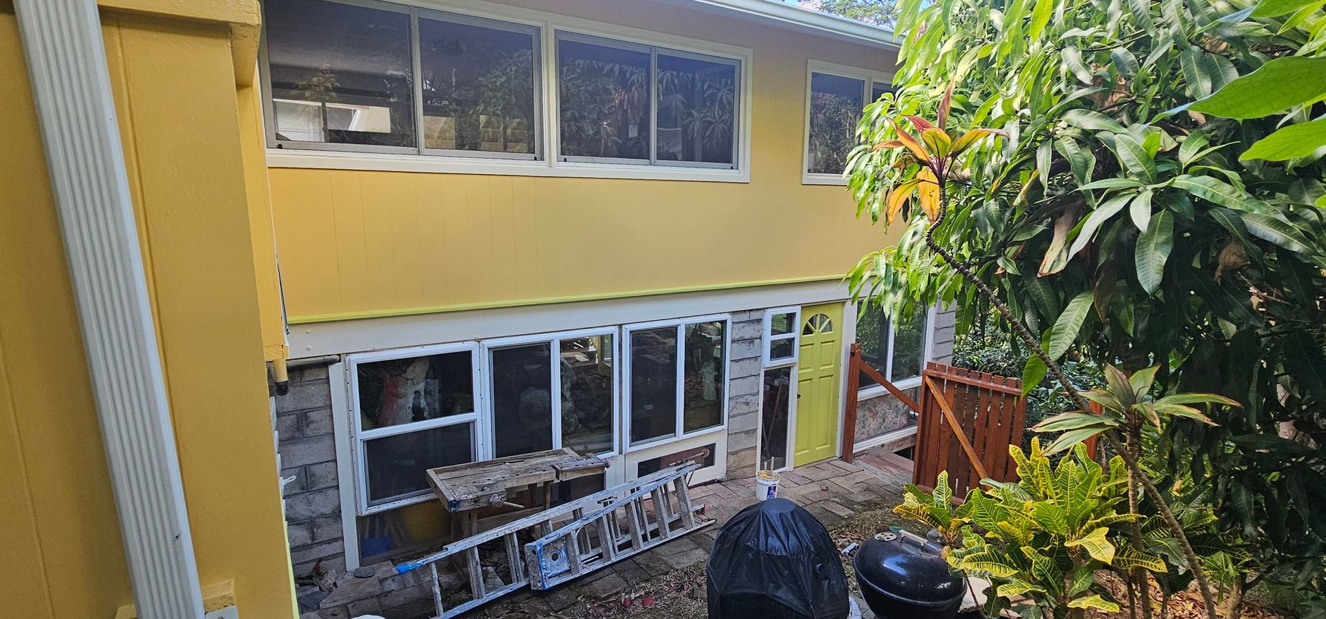 A yellow house with a lot of windows is being painted.