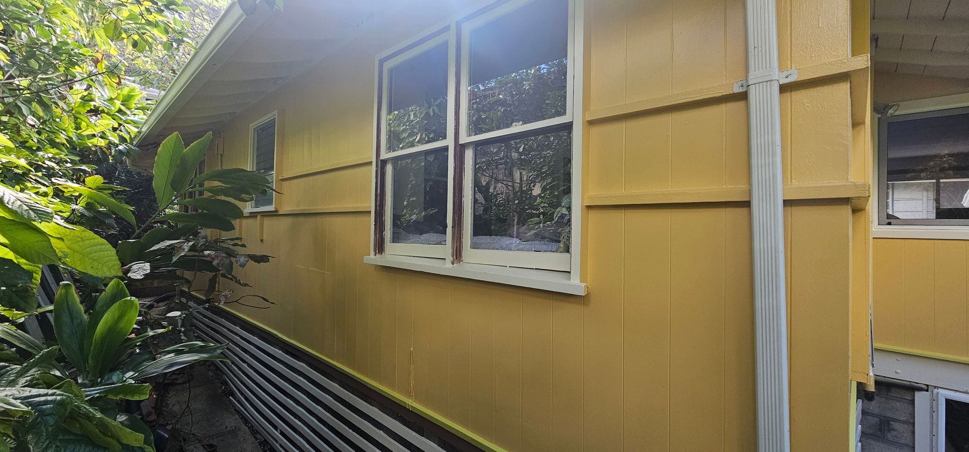 The side of a yellow house with two windows and a gutter.