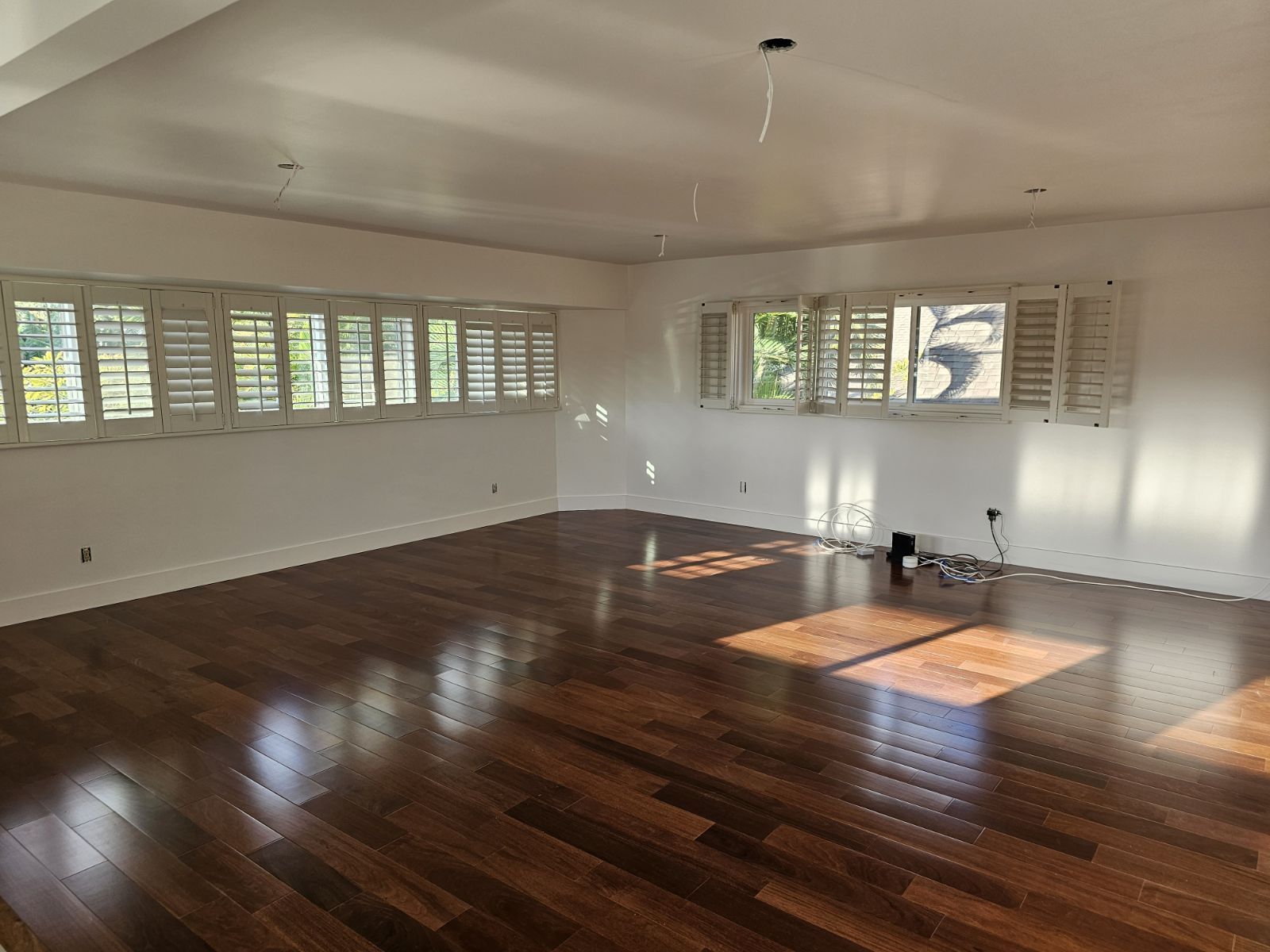 A large empty room with hardwood floors and white shutters on the windows.