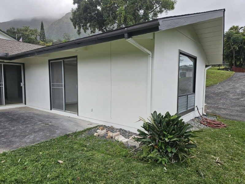 A white house with a sliding glass door is sitting on top of a lush green hillside.