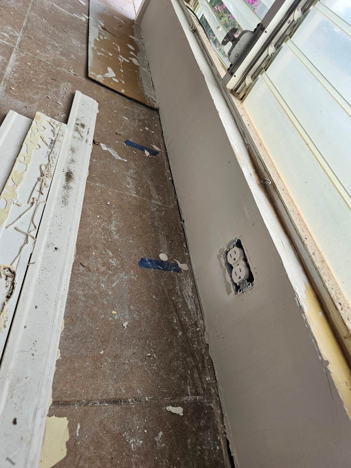 A wall with a electrical outlet and a window in the background
