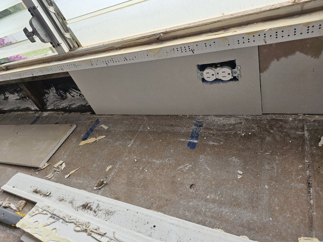 A dirty room with a window and a socket on the wall.