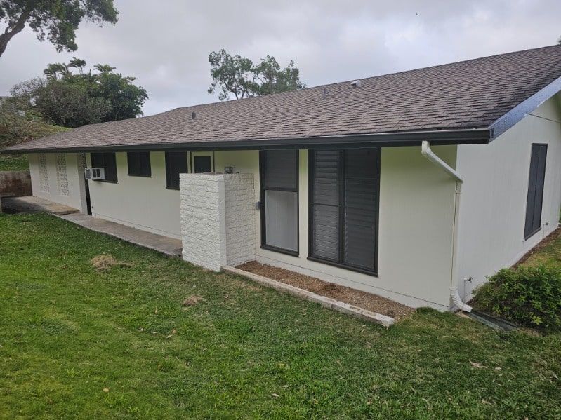 A white house with a brown roof is sitting on top of a lush green lawn.