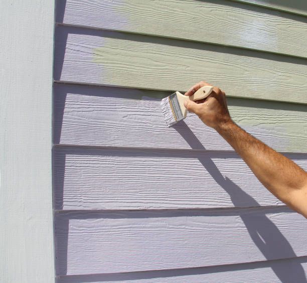 A person is painting the side of a house with a brush.