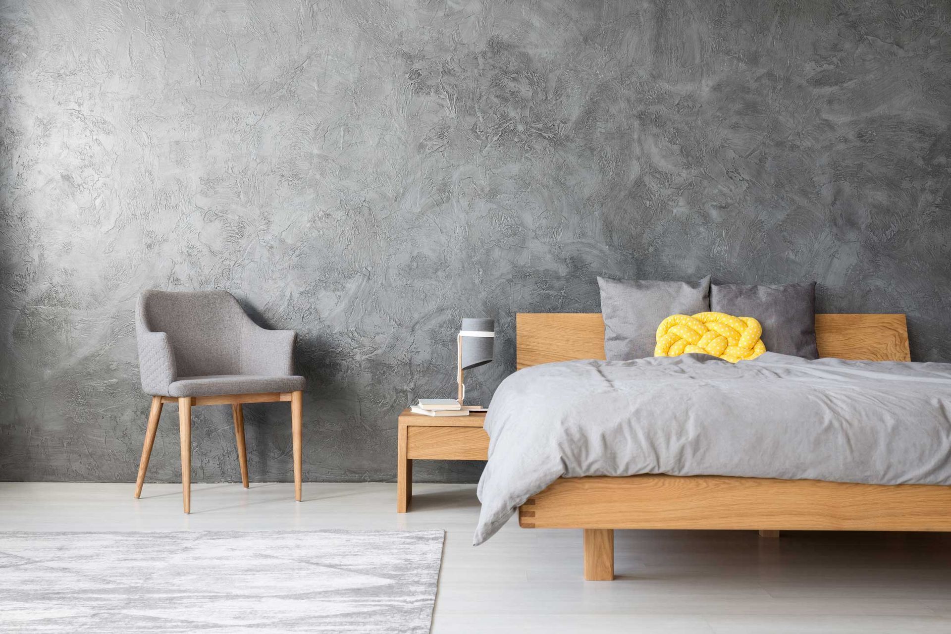 A bedroom with a bed, chair, nightstand and concrete wall.