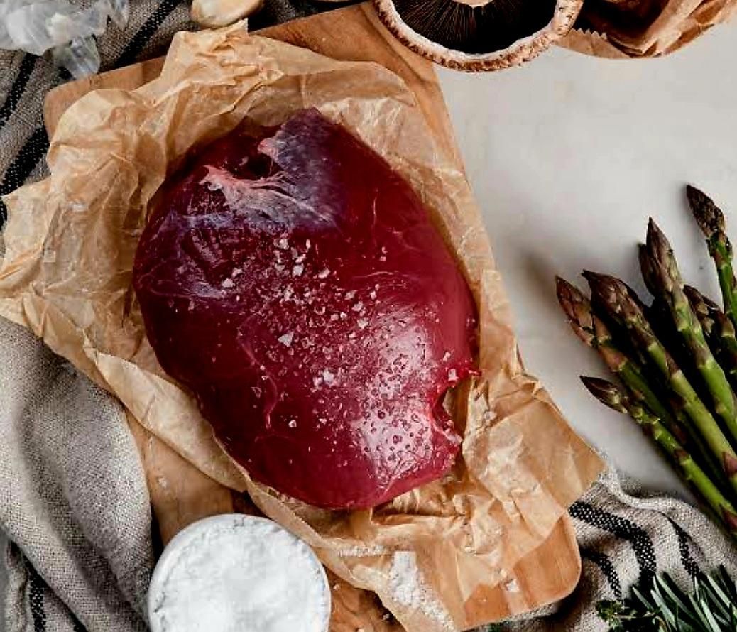 A Large Piece of Red Meat is Sitting on a Piece of Brown Paper Next to Asparagus — Multy Cut Meats In Yorkeys Knob, QLD