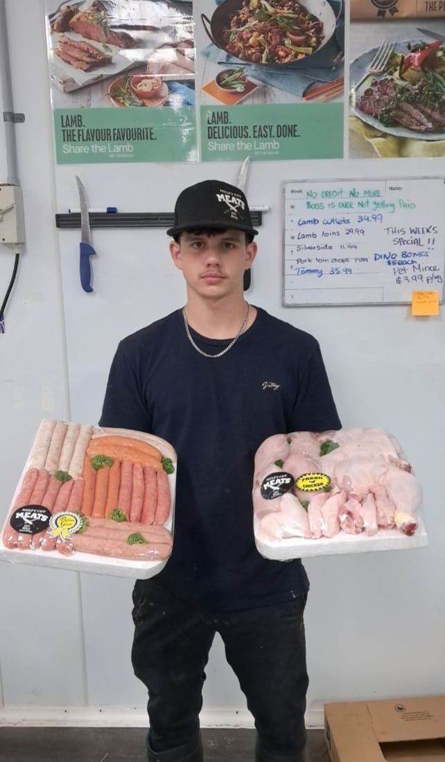 A Man is Holding Two Trays of Meat in Front of a White Board — Multy Cut Meats In Yorkeys Knob, QLD