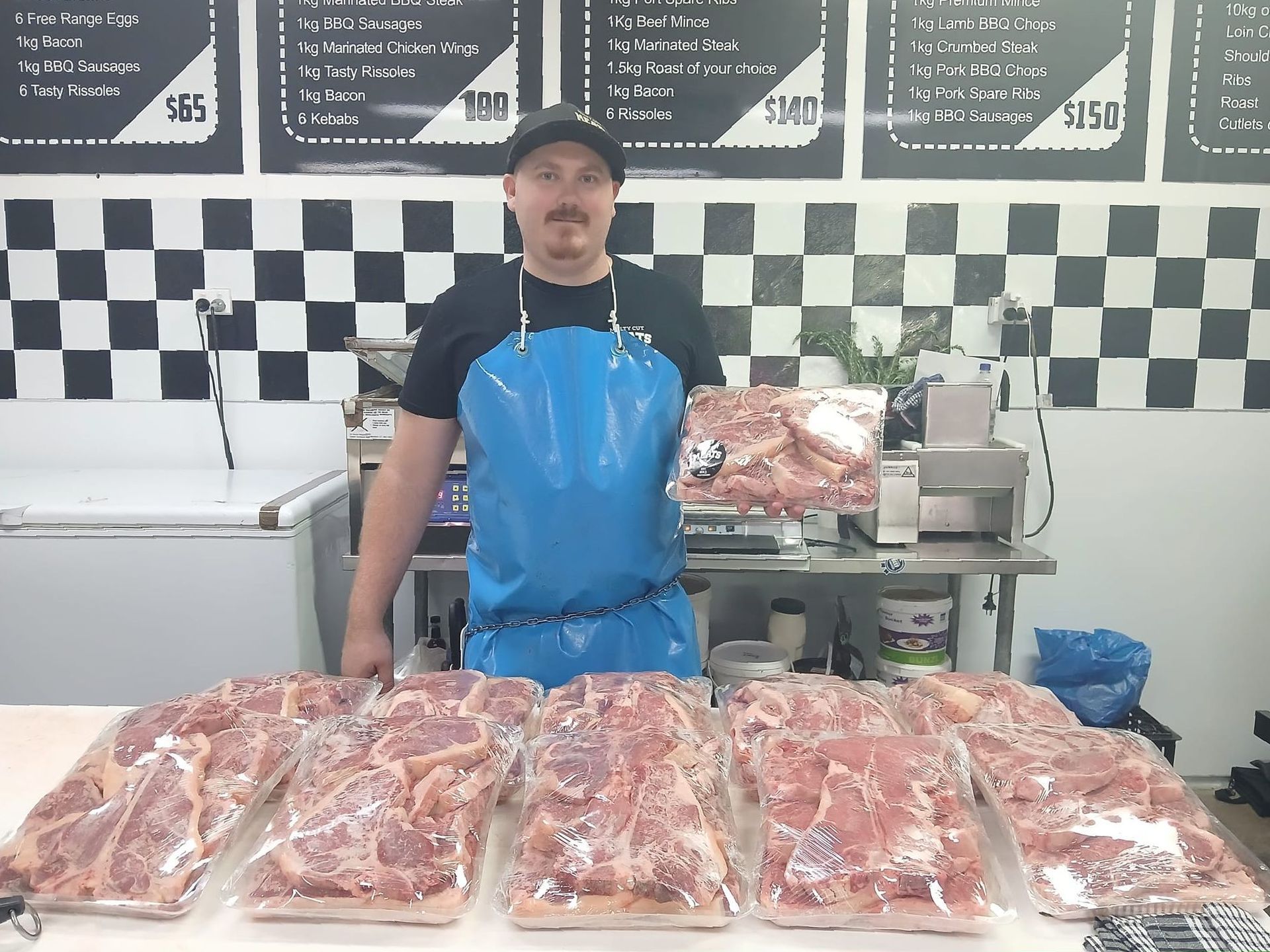 A Man In A Blue Apron Is Holding A Piece Of Meat — Multy Cut Meats In Yorkeys Knob, QLD