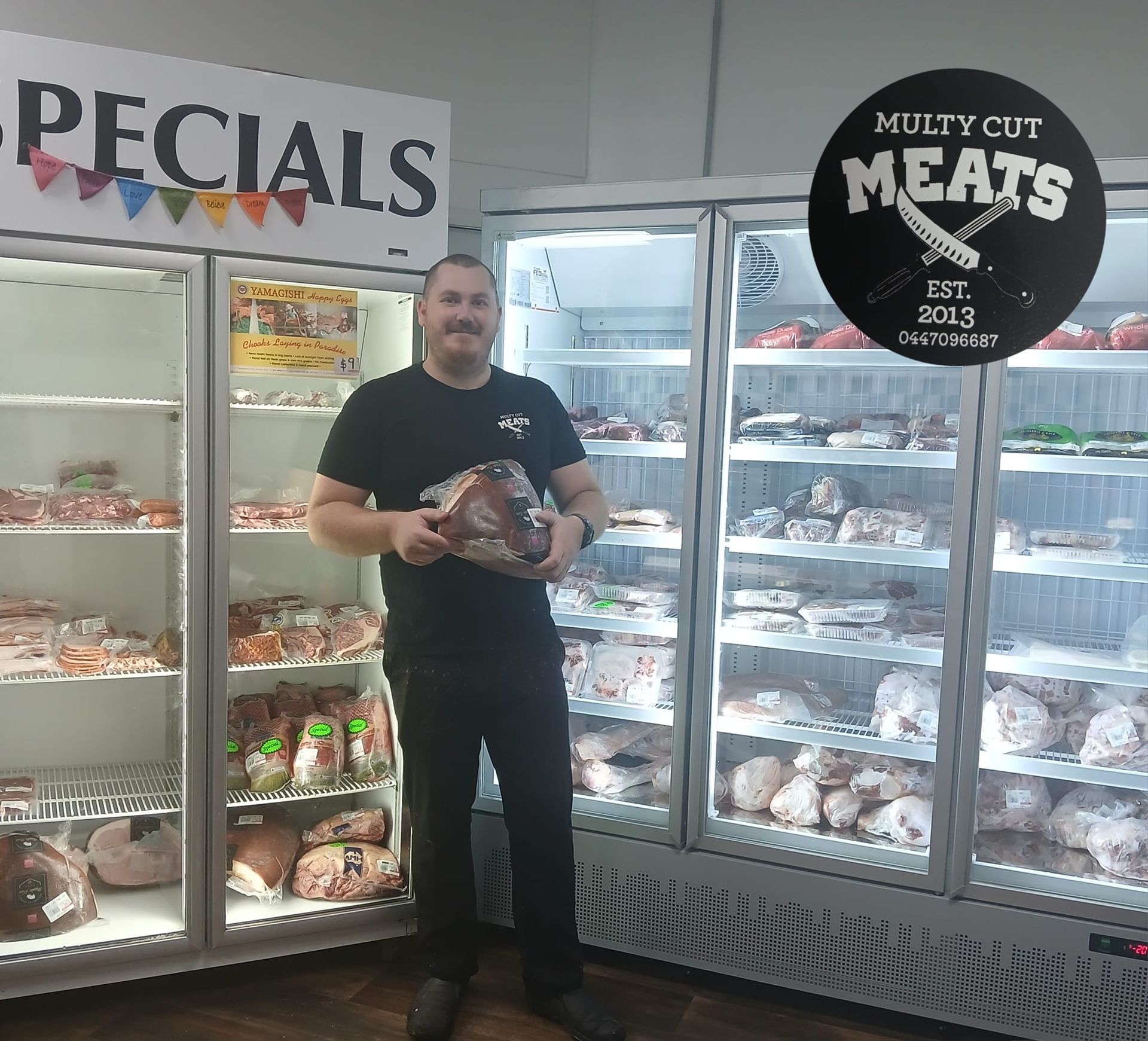 A Man Is Standing In Front Of A Refrigerator That Says Specials — Multy Cut Meats In Yorkeys Knob, QLD