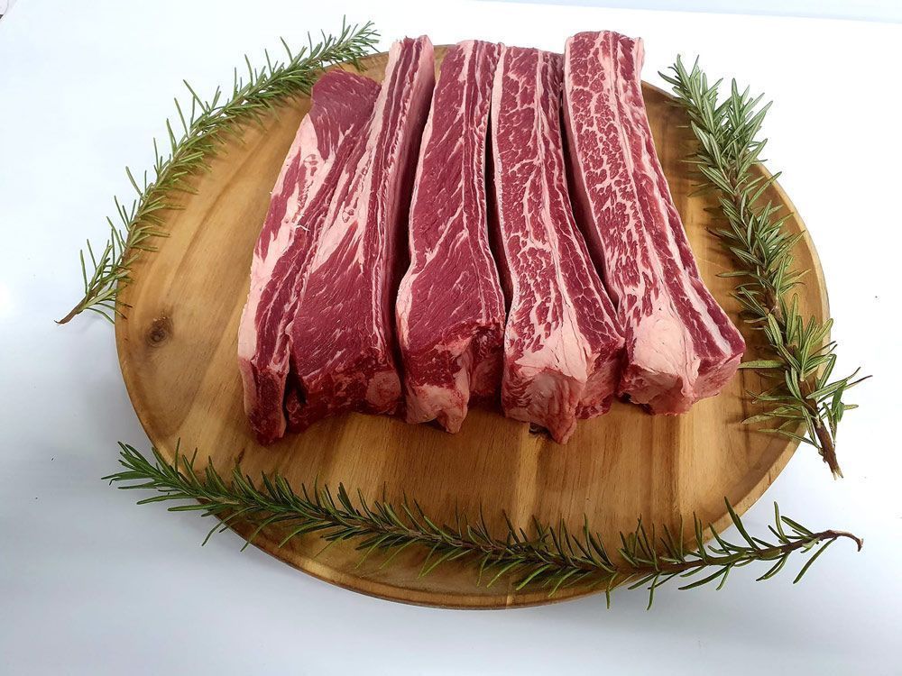 A Wooden Cutting Board Topped With Beef Ribs and Rosemary — Multy Cut Meats In Yorkeys Knob, QLD