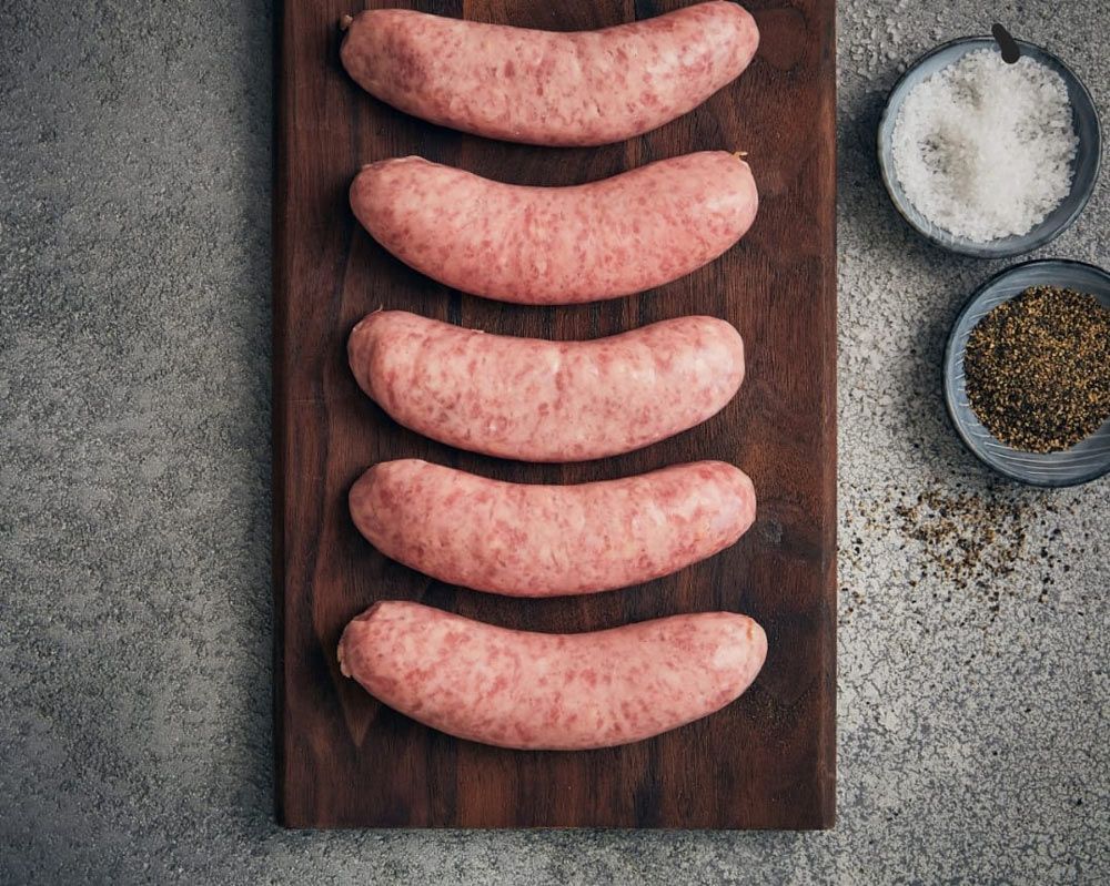 Raw Sausages Are Lined Up on a Wooden Cutting Board — Multy Cut Meats In Yorkeys Knob, QLD