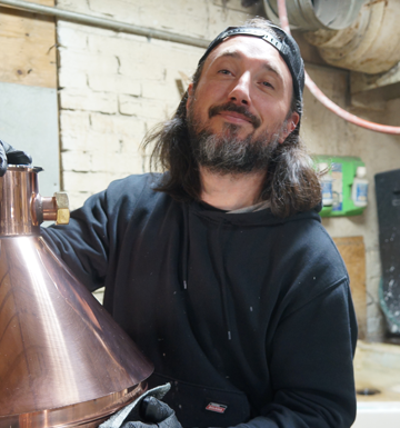 A man with long hair and a beard is standing next to a copper pot