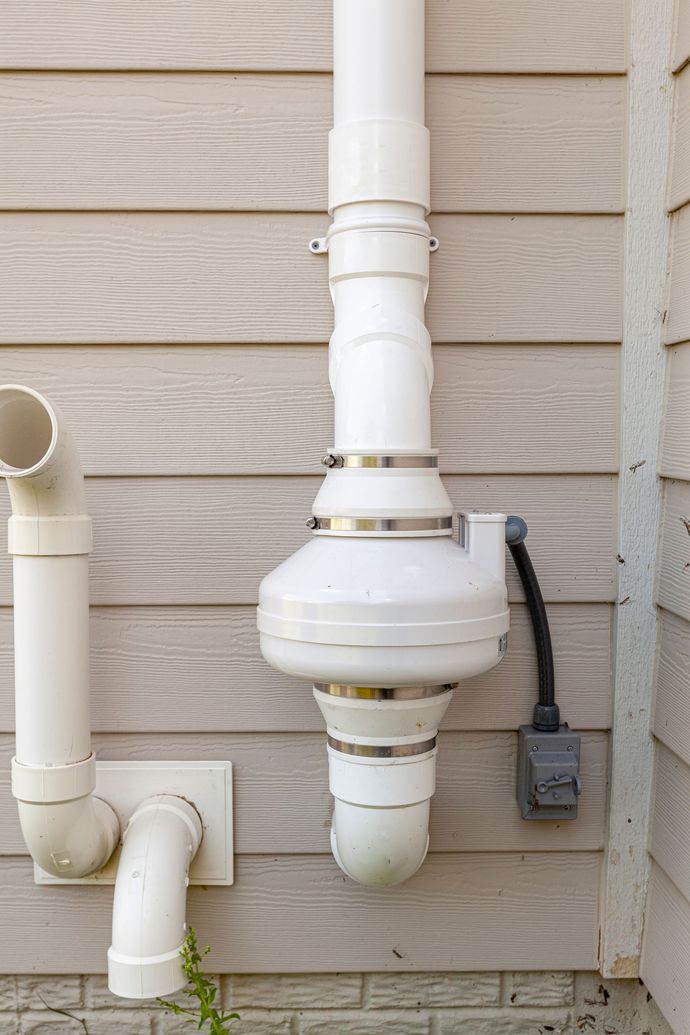 A white pipe is attached to the side of a house.