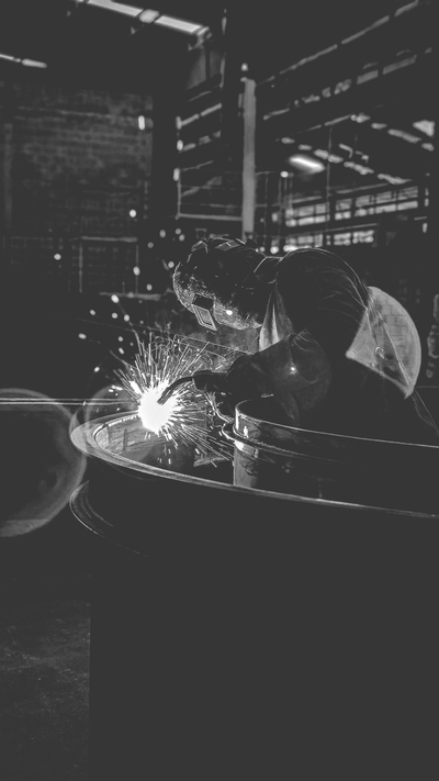 Arbeiders bedienen een lasapparaat in een donkere industriële werkplaats, waarbij vonken in het rond vliegen.