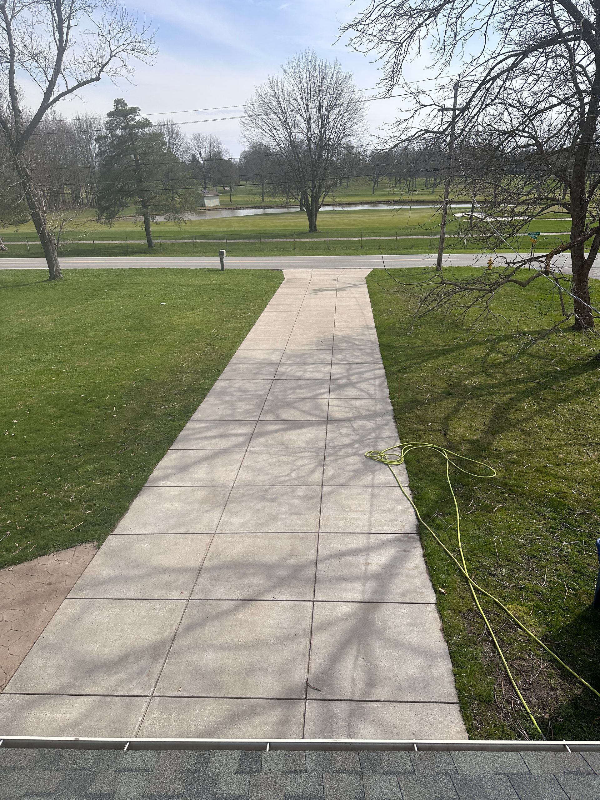 A concrete walkway leading to a grassy field in a park.