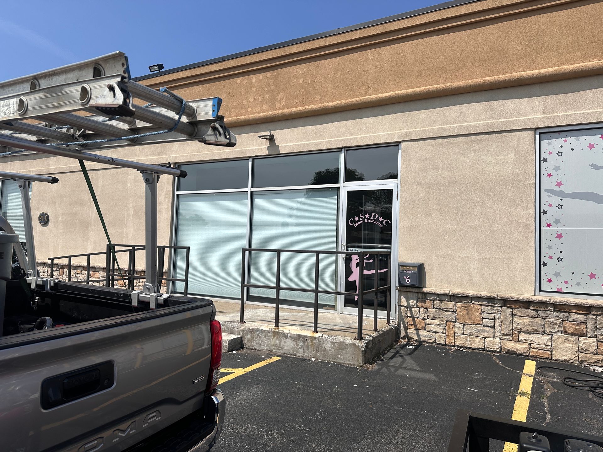 A truck with a ladder in the back is parked in front of a building.