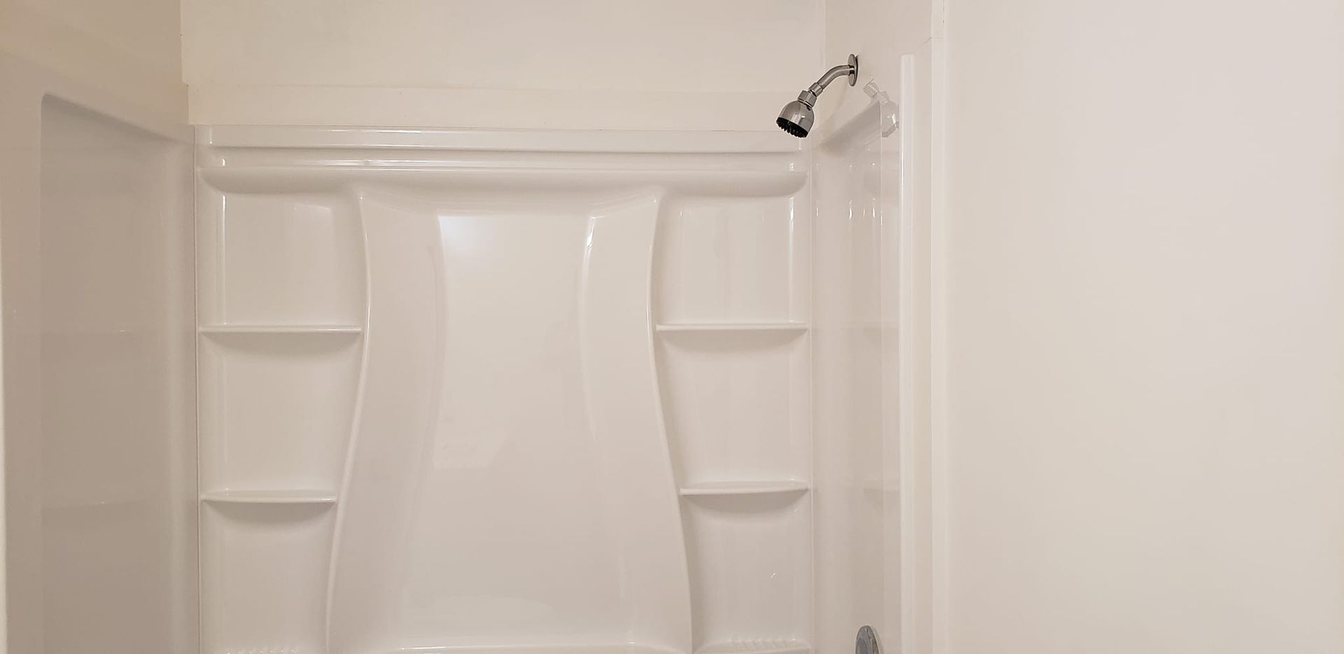 A white shower stall with shelves and a shower head in a bathroom.