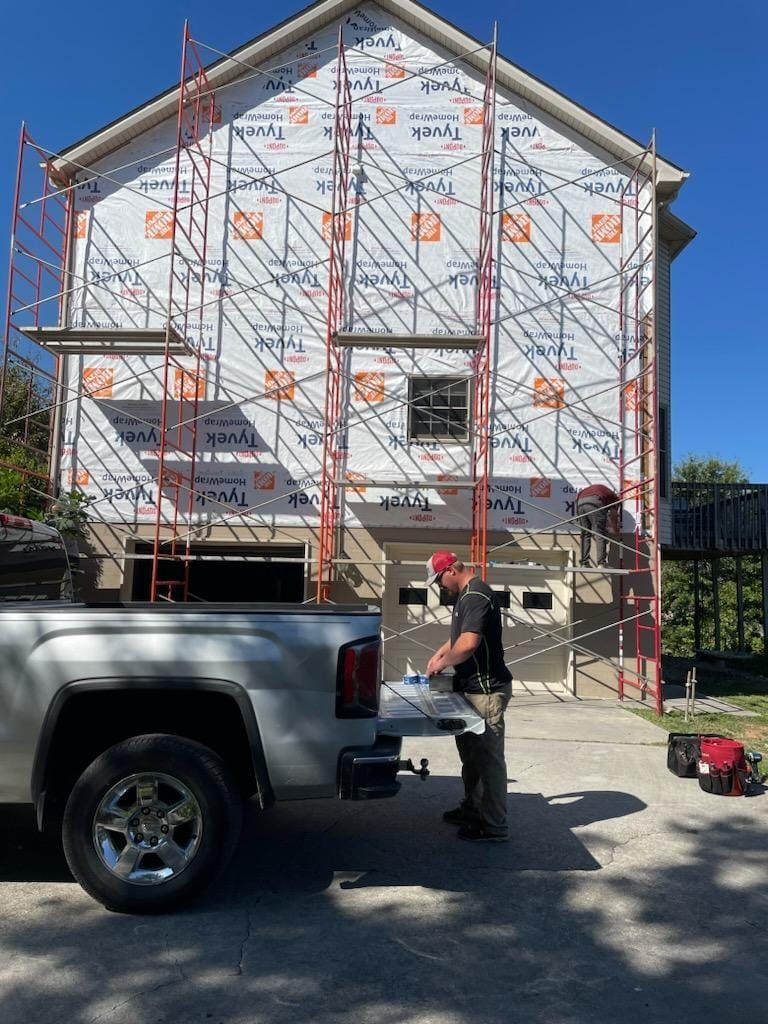 A man is loading something into the back of a truck in front of a house under construction.