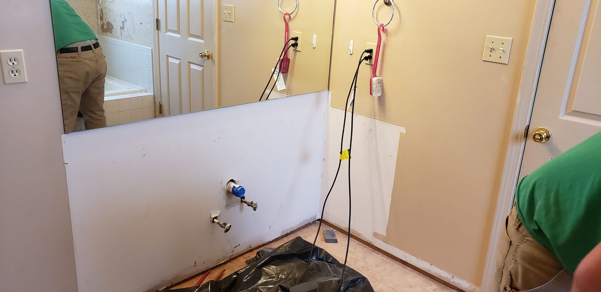 A man is standing in a bathroom next to a large mirror.