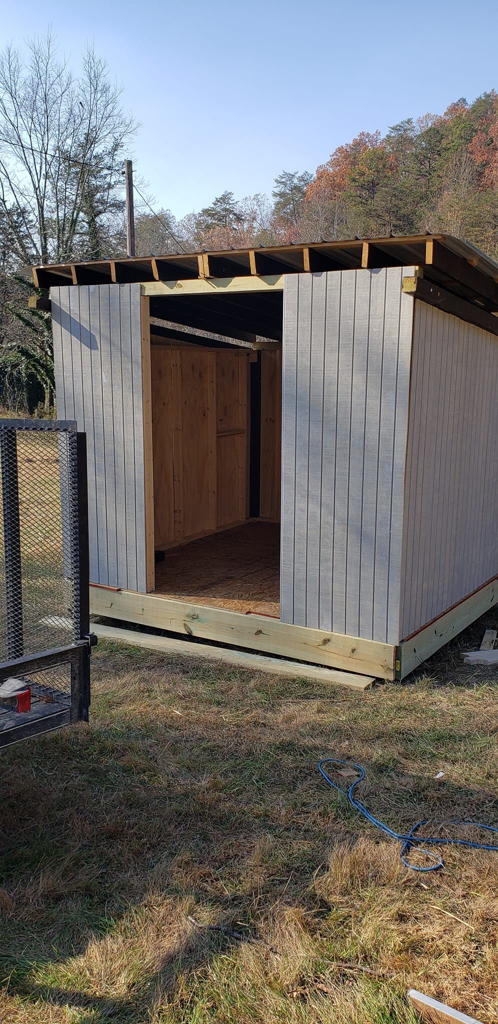 A small wooden shed is sitting in the middle of a grassy field.