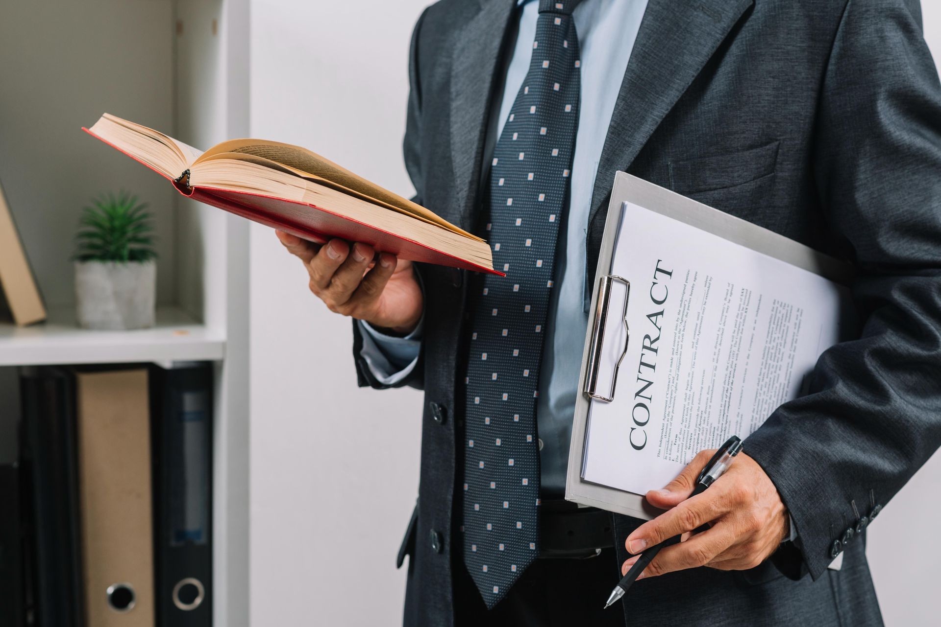 A man in a suit and tie is holding a clipboard and a book.