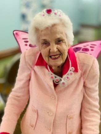 An elderly woman wearing a pink jacket and pink wings
