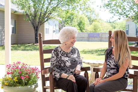 Two women are sitting on a porch talking to each other.