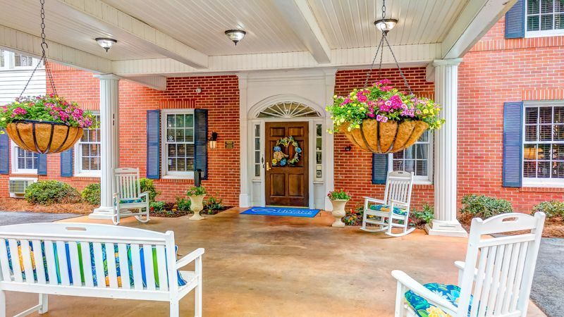 A porch with a bench and rocking chairs in front of a brick building.
