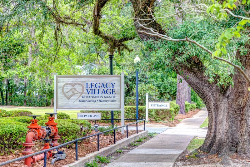 A sign for legacy village is sitting on the sidewalk next to a tree.