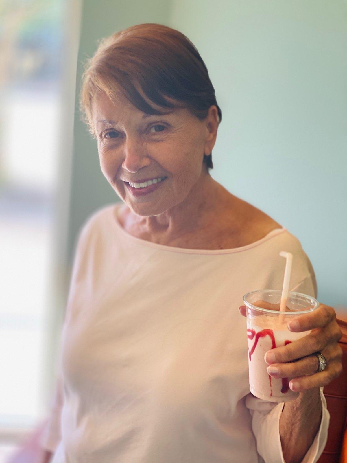 A woman is holding a milkshake with a straw in her hand.