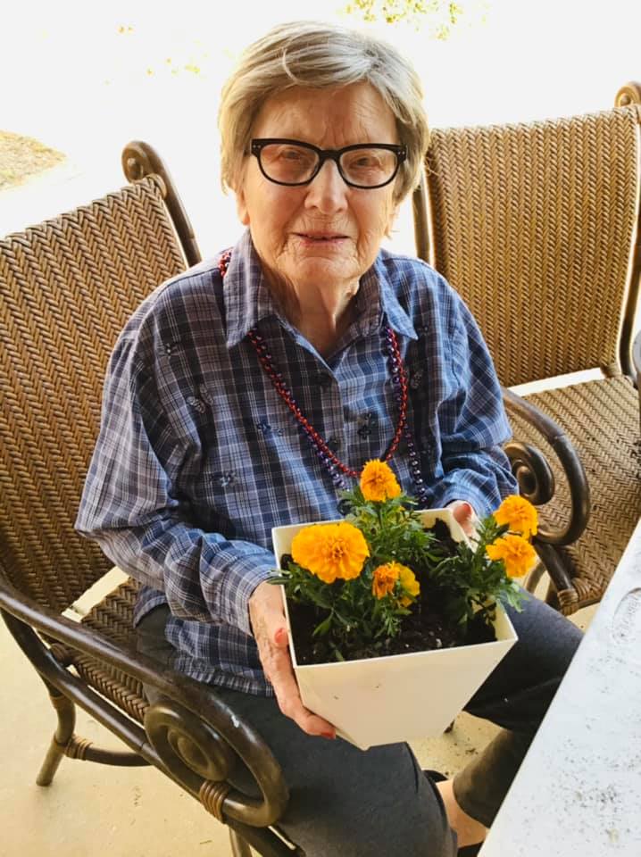 An elderly woman is sitting in a chair holding a pot of flowers.