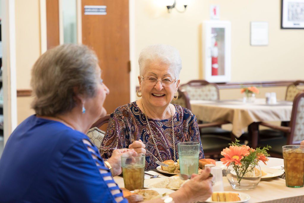 Two elderly women are sitting at a table eating food.