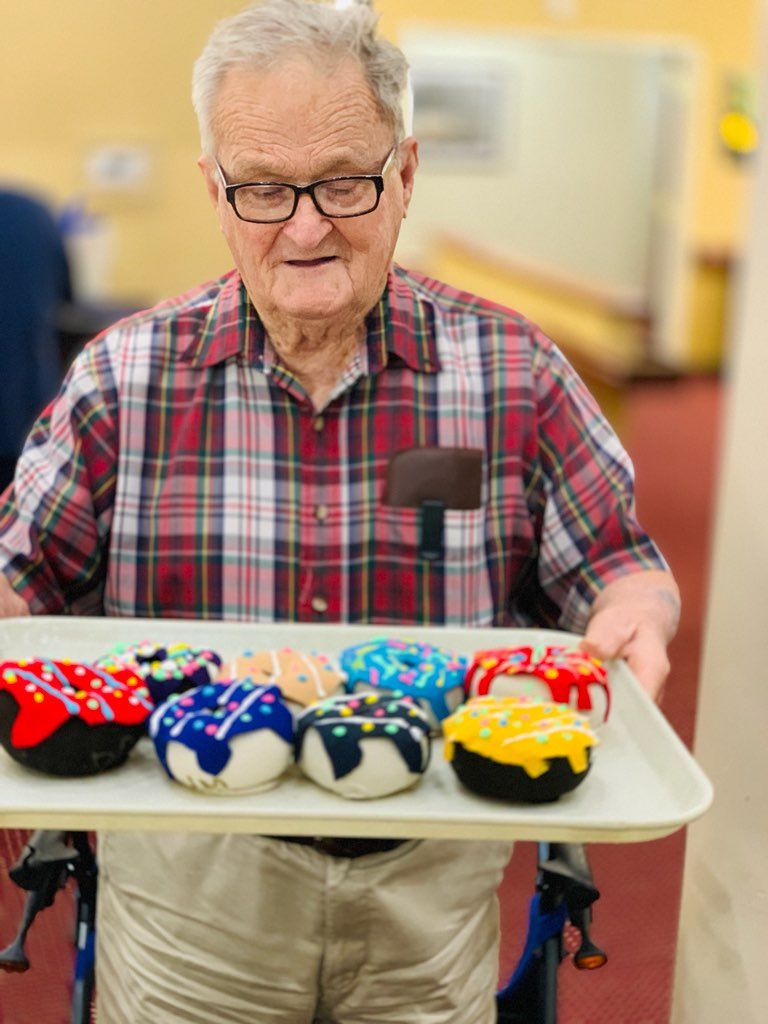 An elderly man in a wheelchair is holding a tray of donuts.