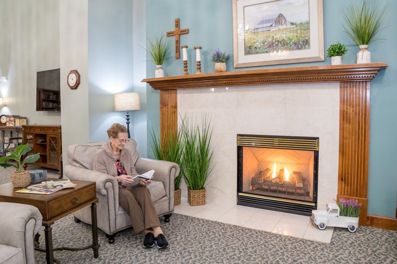 A woman is sitting in a chair in front of a fireplace in a living room.