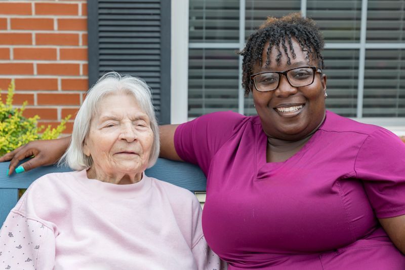 A nurse is sitting next to an elderly woman on a bench.