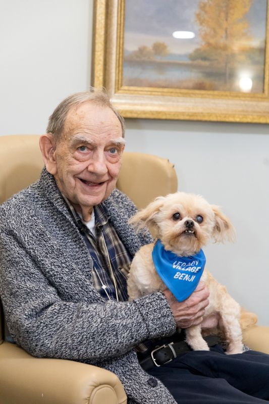 An elderly man is sitting in a chair holding a small dog.