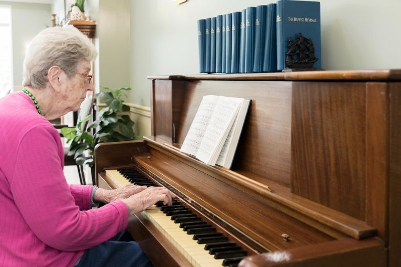 An elderly woman is playing a piano in a living room.