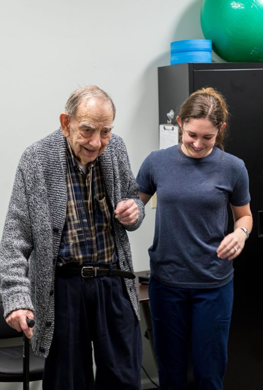 A woman is helping an older man walk with a cane.