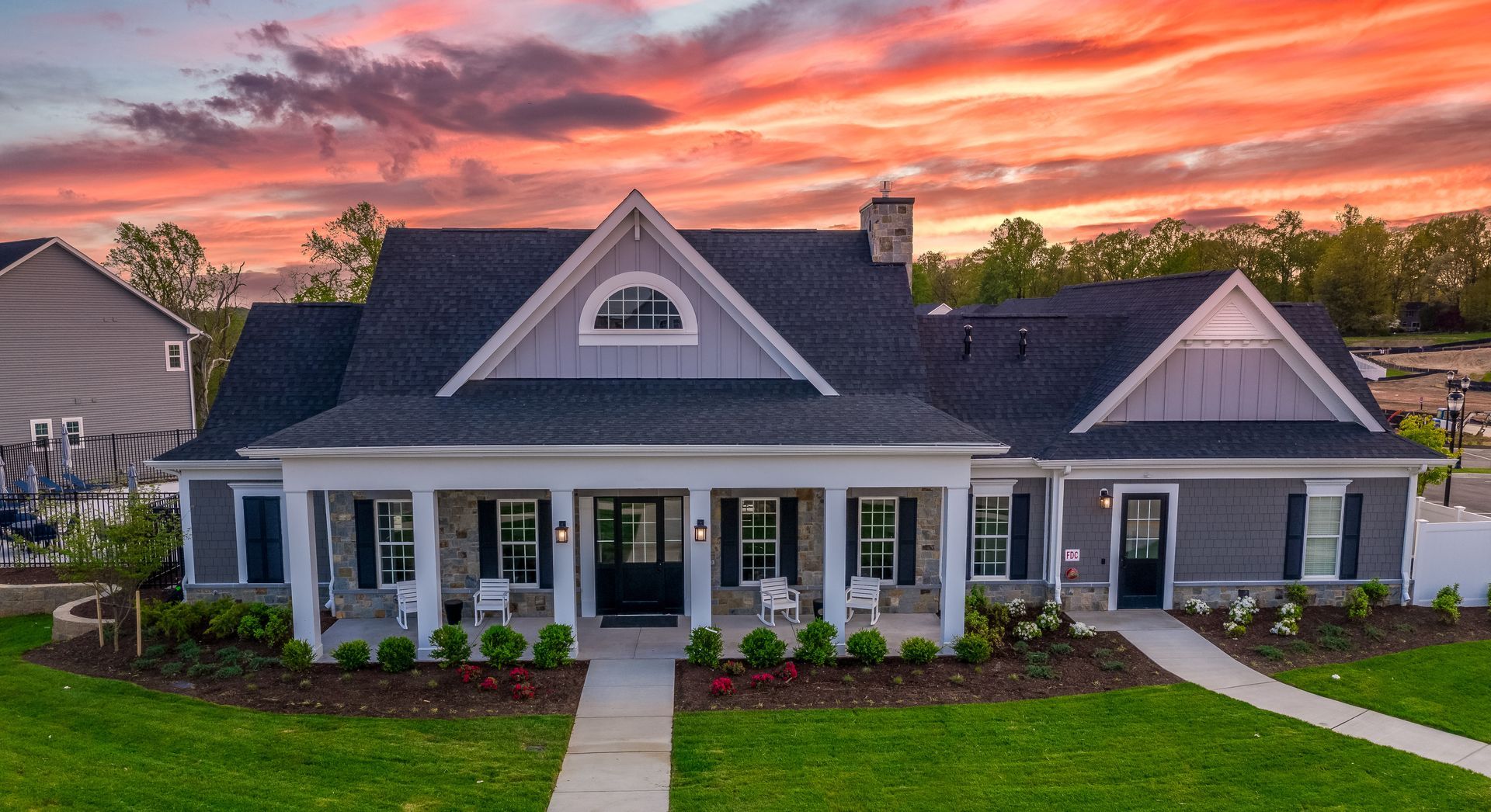 Cottage-style home with covered porch, gray siding, and a vibrant sunset sky.