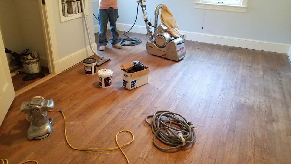 A man is sanding a wooden floor in a room.