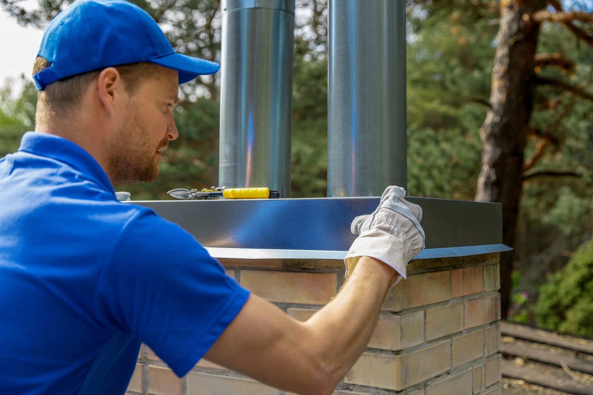 Worker in blue shirt and cap measuring a brick chimney with a level outdoors Worker in blue shirt and cap measuring a brick chimney with a level outdoors