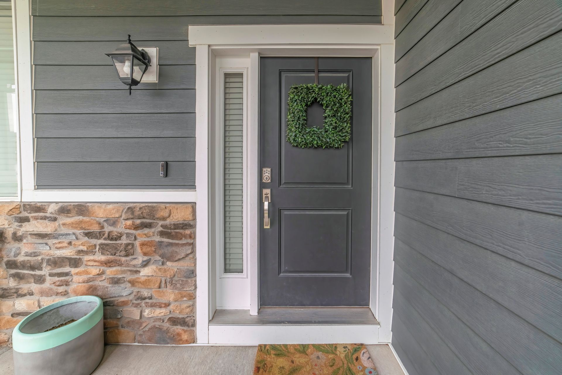 Front porch with gray front door, wreath, wall lantern, stone accent wall, and planter.