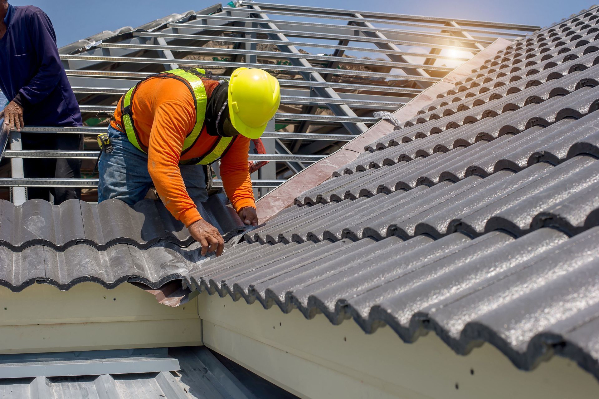 Worker in orange vest and yellow hard hat repairs a corrugated roof during construction. Worker in orange vest and yellow hard hat repairs a corrugated roof during construction.