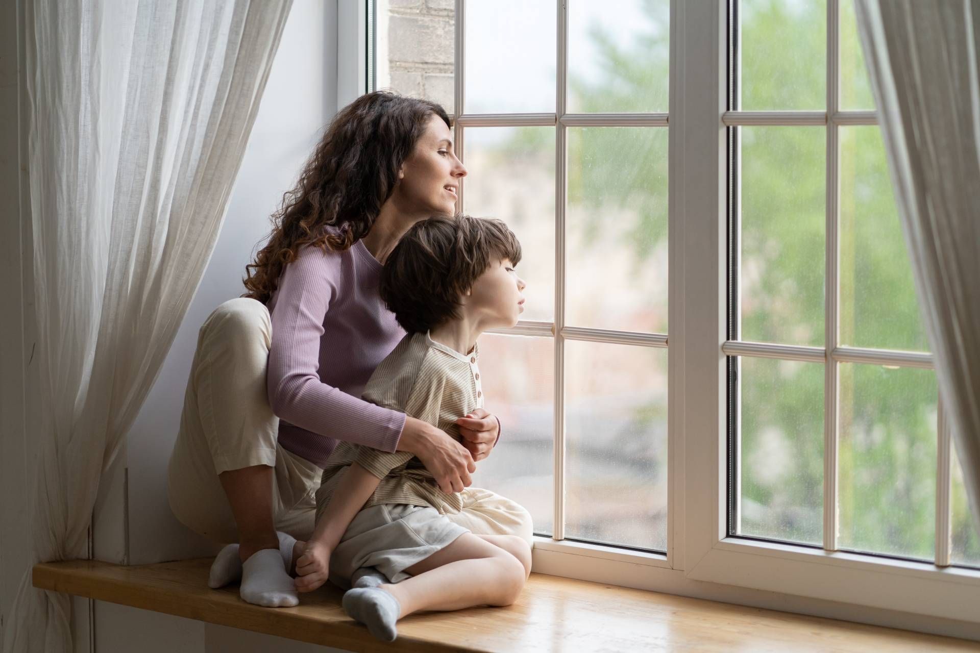 A parent and child sitting on a window sill looking out near Greenville, South Carolina (SC)