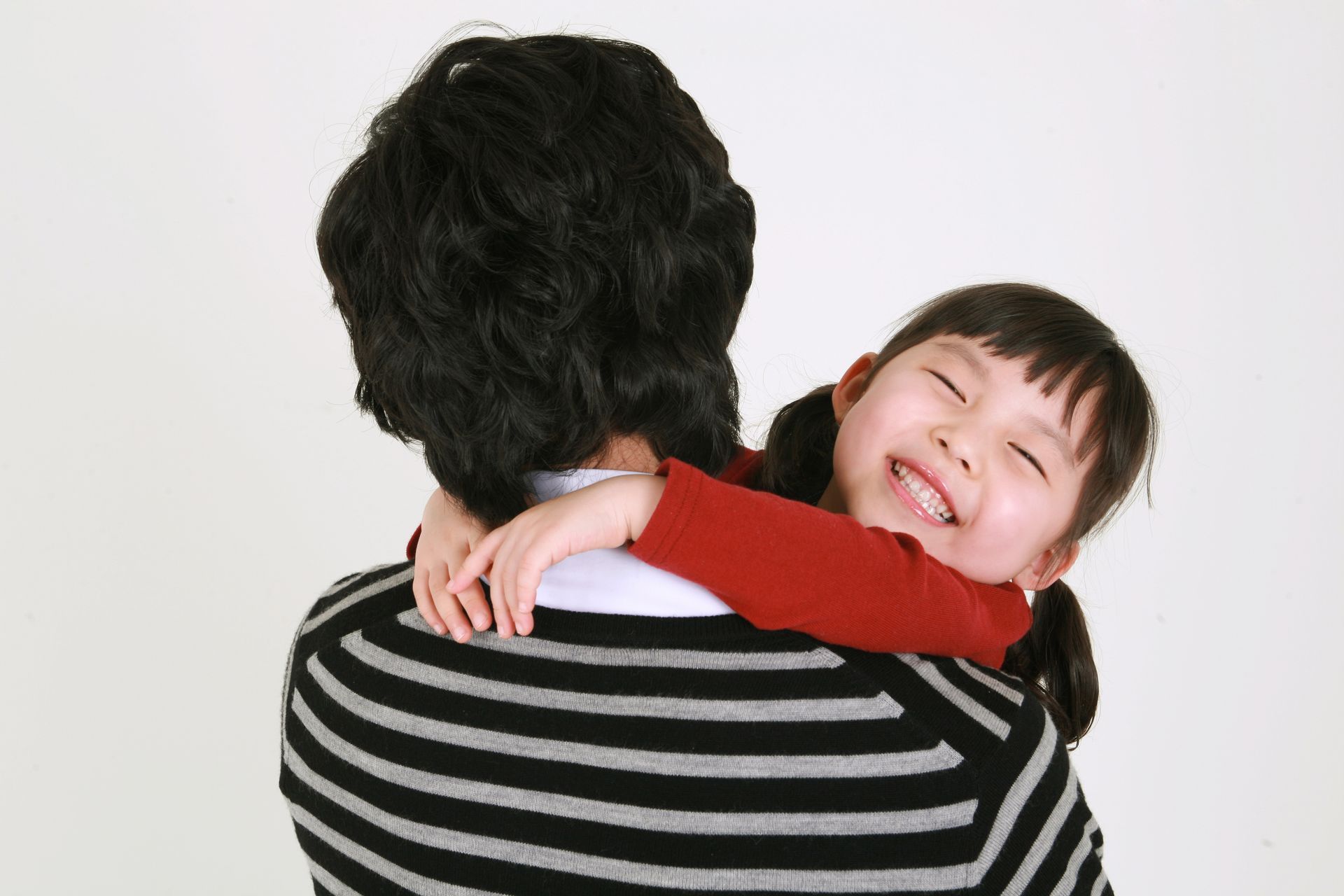 Child hugging a person from behind, smiling; black and white striped shirt.