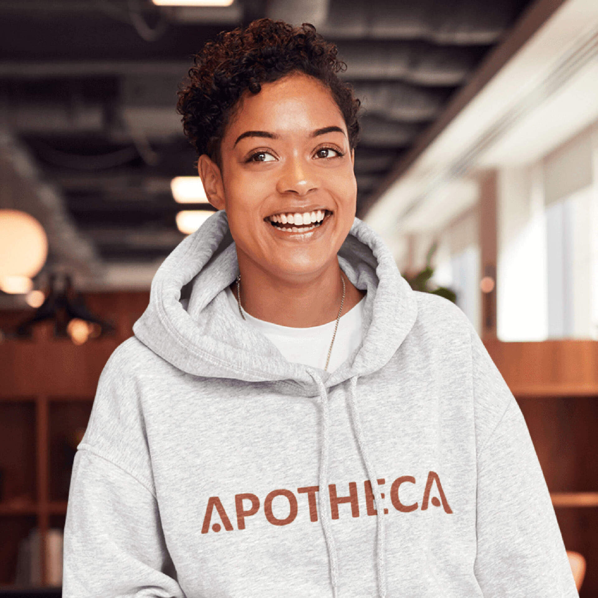 A woman wearing a grey apotheca hoodie is smiling.