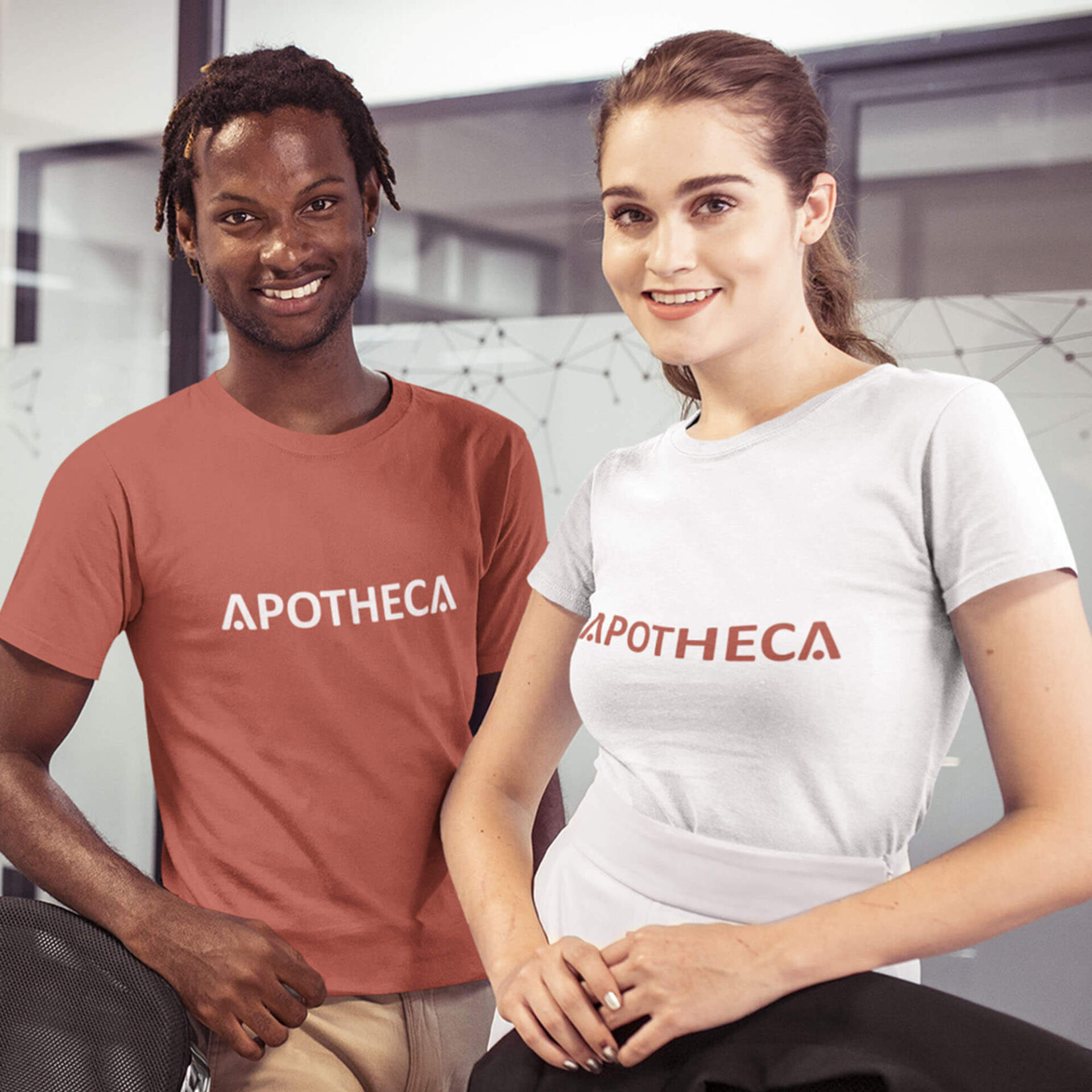 A man and a woman are standing next to each other wearing apotheca shirts.