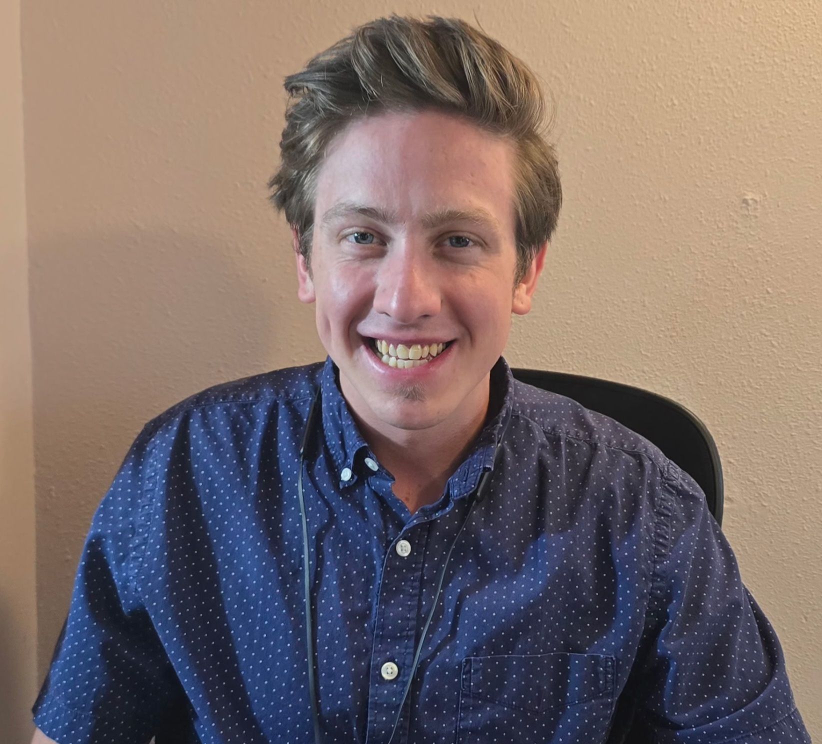 A young man in a blue shirt is smiling for the camera